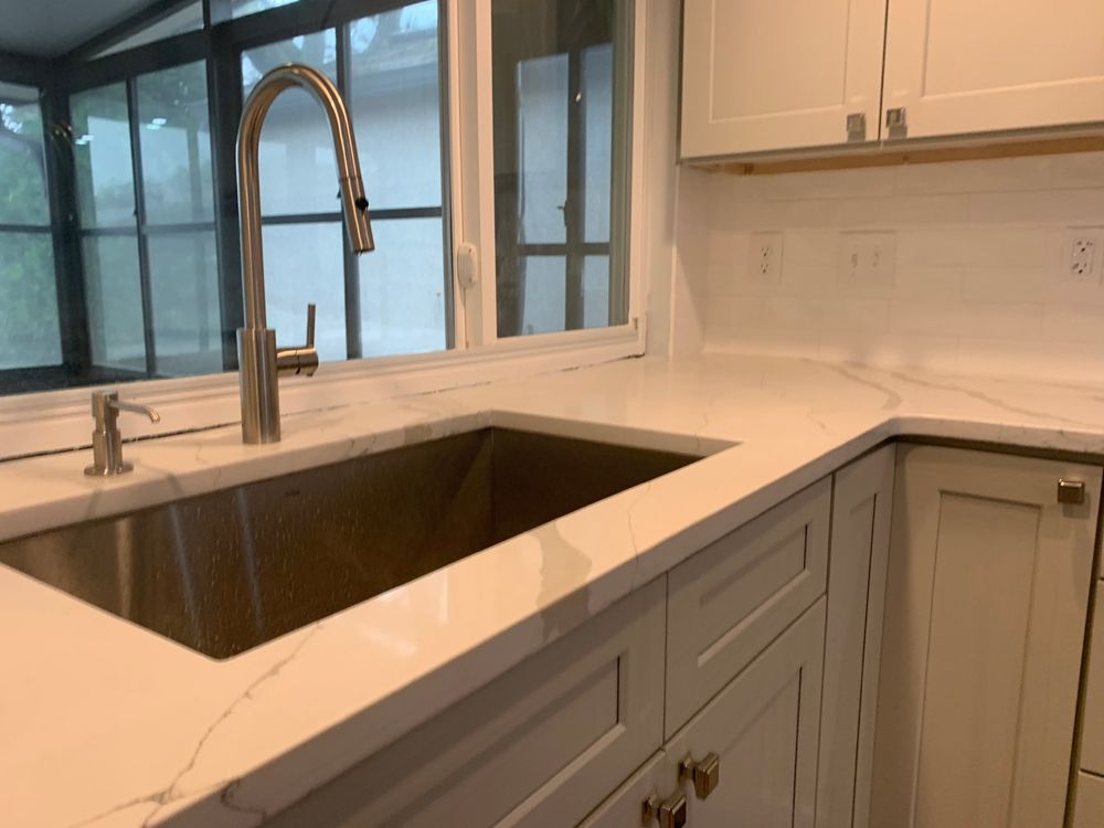Modern kitchen with stainless steel sink, white cabinets, and marble countertop.