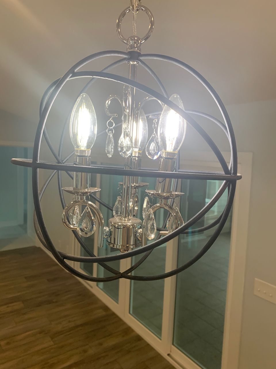 Orb-shaped chandelier with three lit bulbs, silver accents, and hanging crystals, indoors.