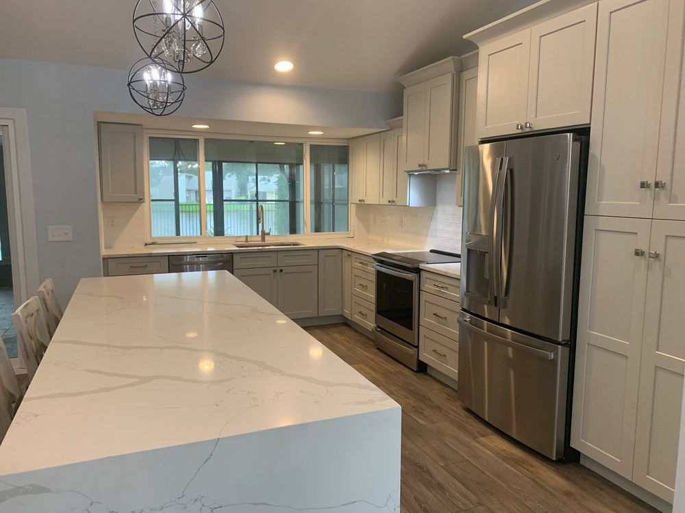 Modern kitchen with white cabinets, large island, stainless steel appliances, and light wood floors.