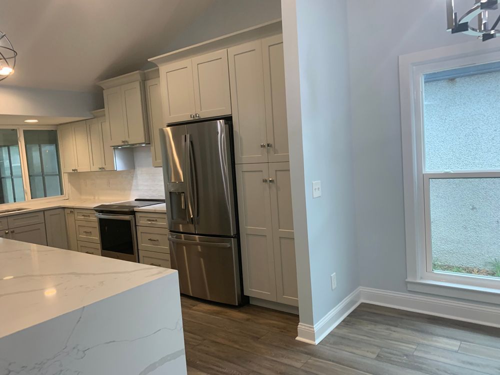 Modern kitchen with white cabinets, stainless steel refrigerator, and a light blue wall next to a window.