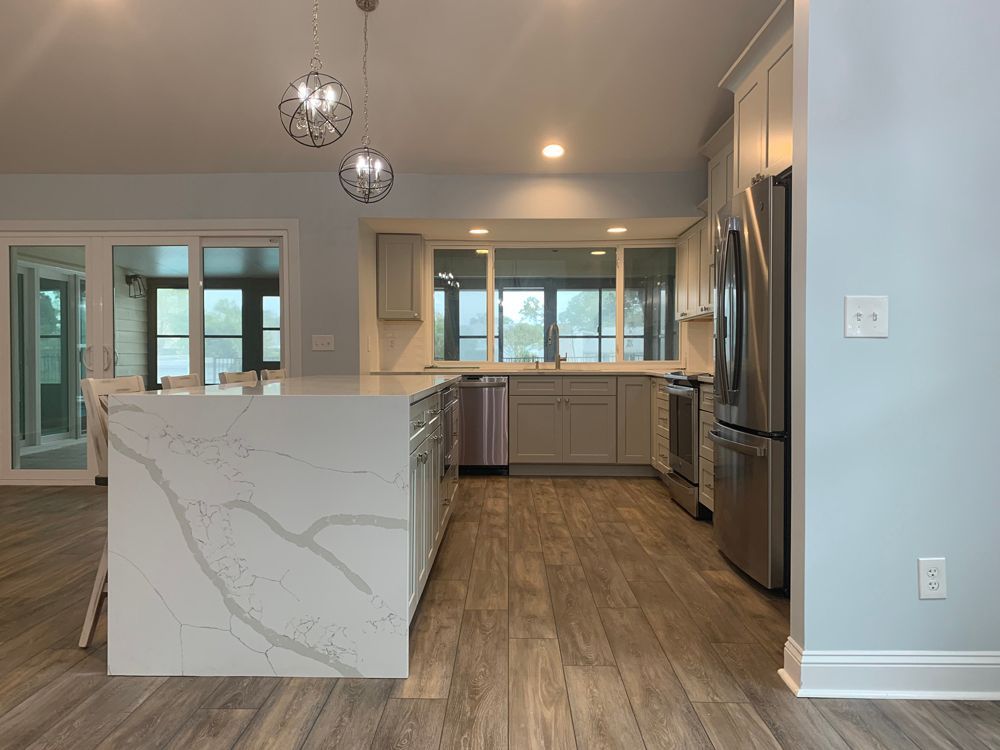 Modern kitchen with white island, light gray cabinets, stainless steel appliances, and light blue walls.