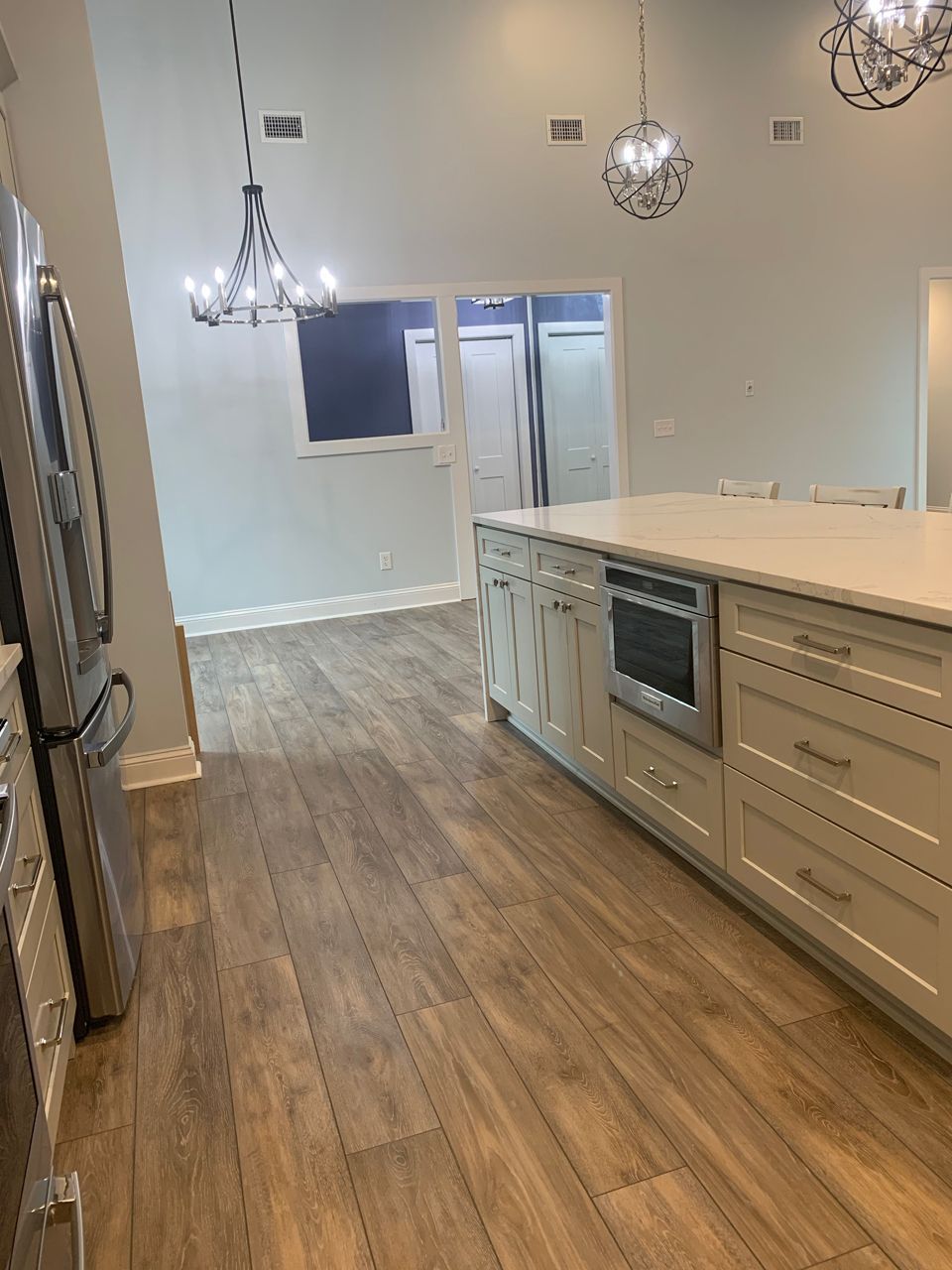 Spacious kitchen with island, light wood floors, pale blue walls, stainless steel appliances, and two chandeliers.