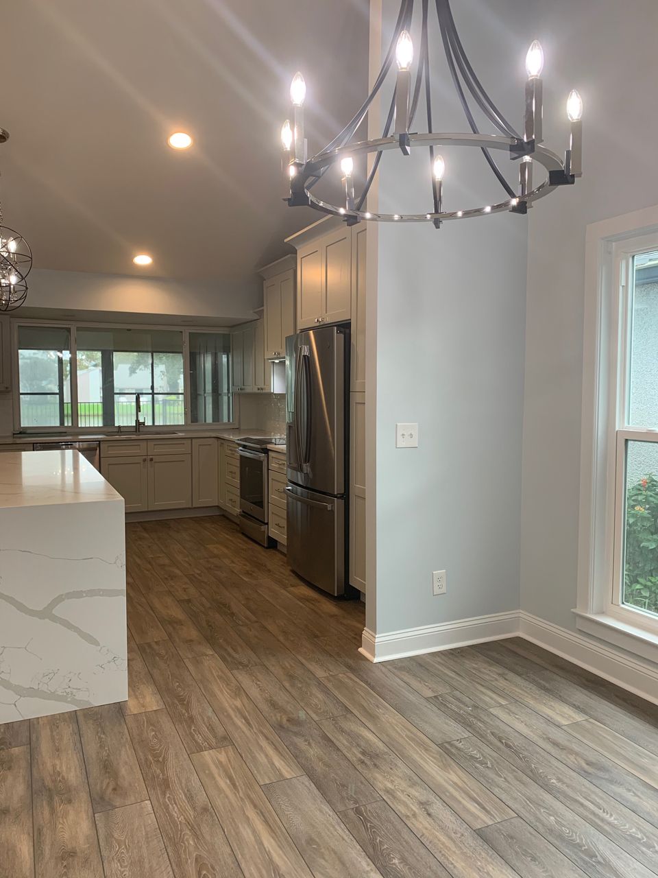 Modern kitchen with wood floors, light gray cabinets, stainless steel appliances, and a chandelier.
