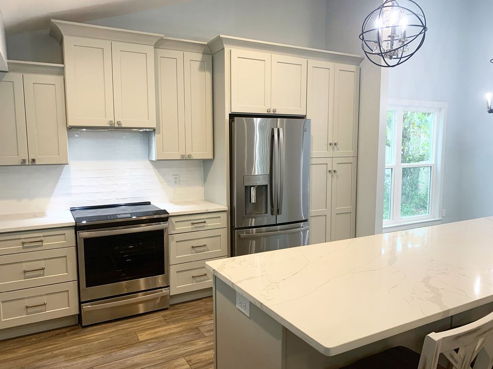 Modern kitchen with light gray cabinets, stainless steel appliances, and white countertops.