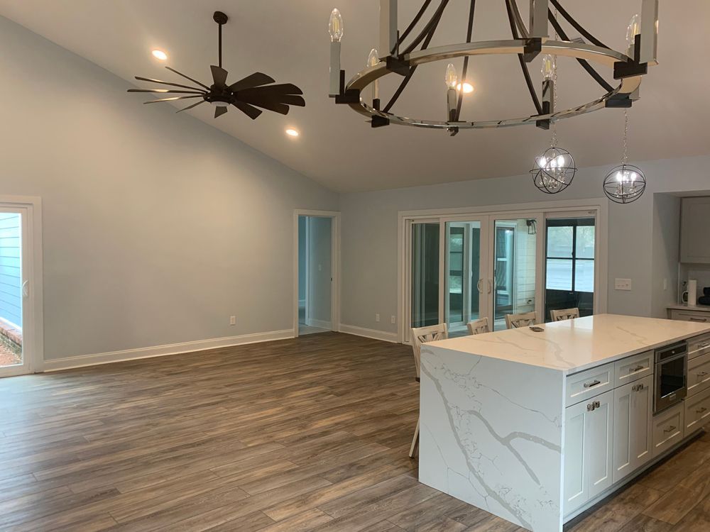 Open-concept living space with kitchen island, light wood floors, light blue walls, and decorative lighting.