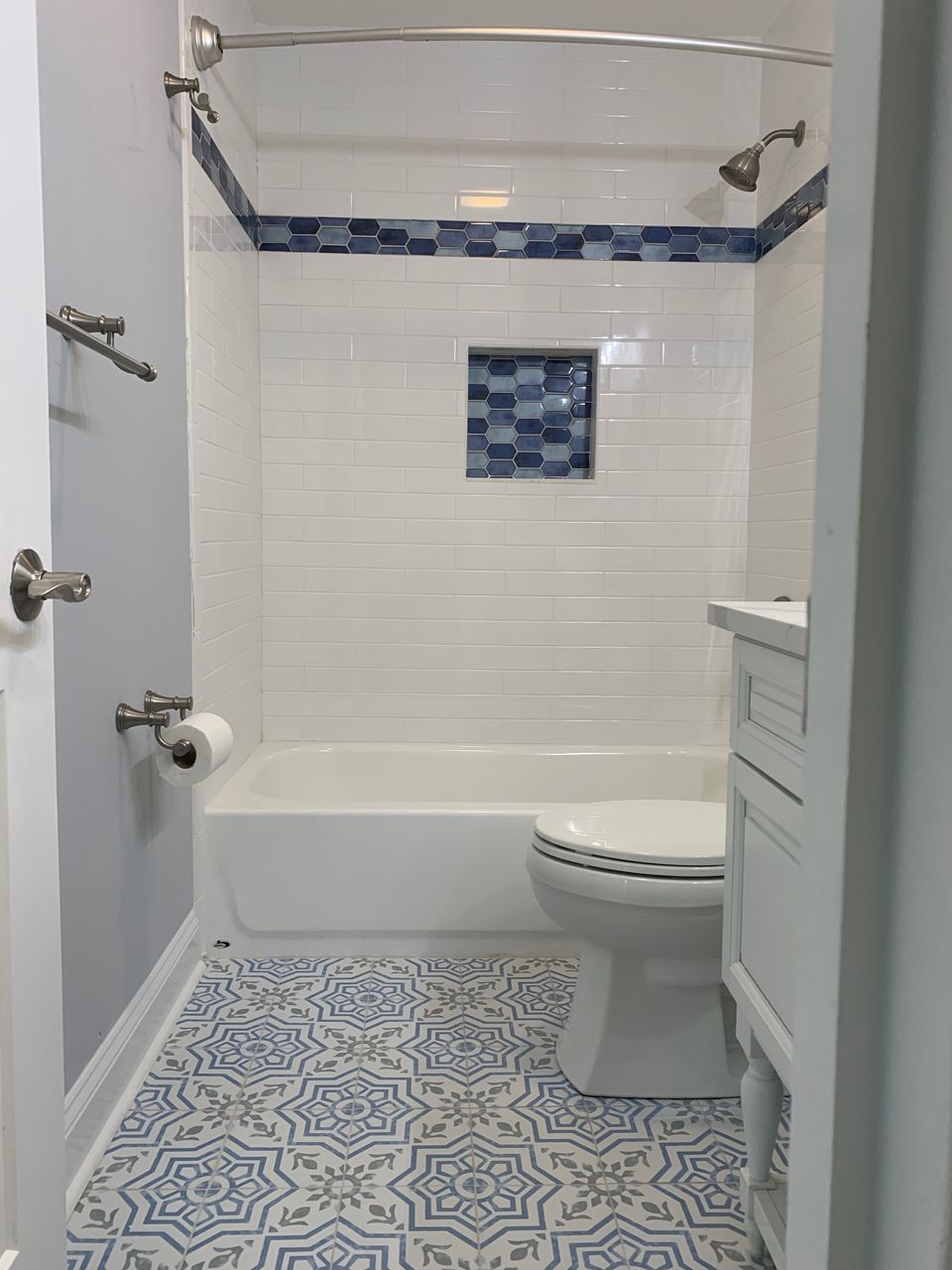 Bathroom with white tub, blue mosaic tile accents, and patterned blue and white floor.