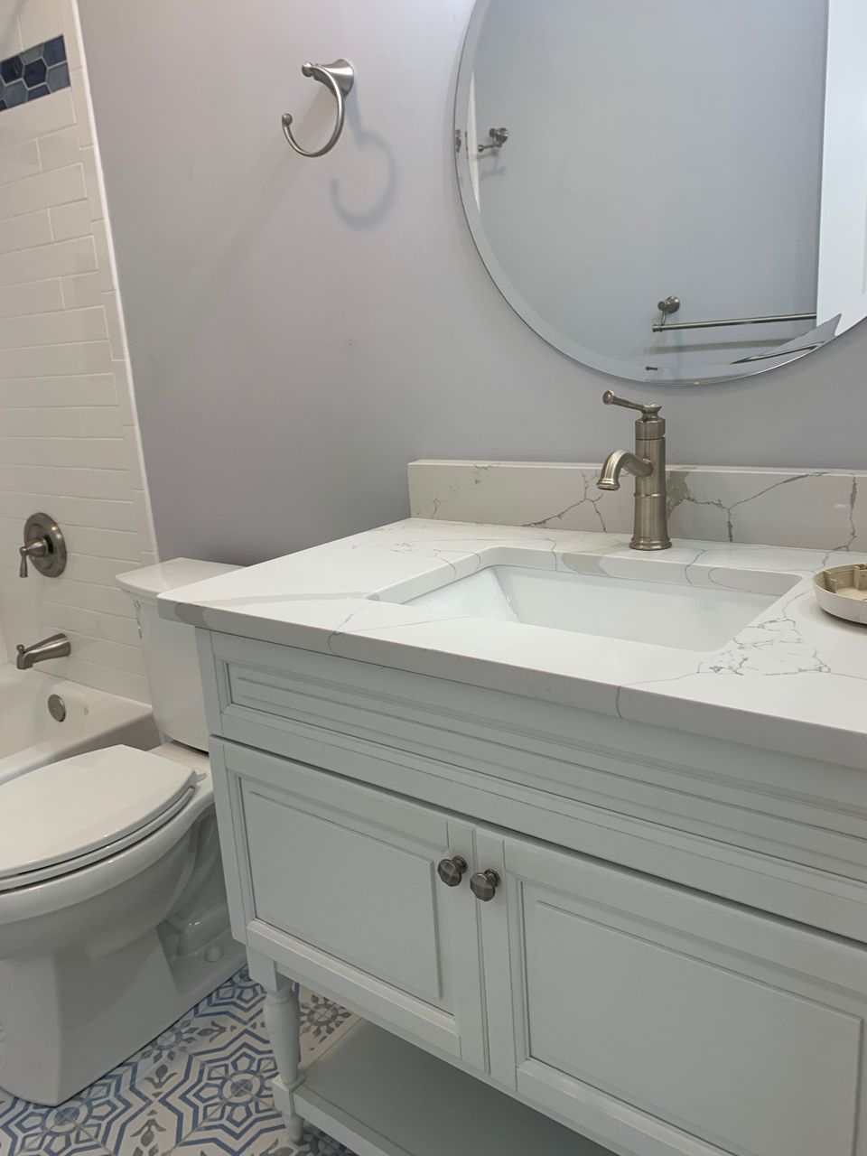 White bathroom vanity with marble countertop, round mirror, and blue patterned floor.