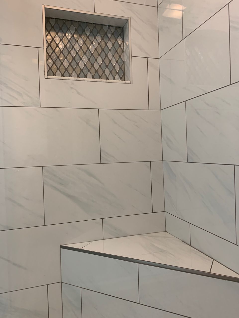 White tiled shower with built-in corner seat and decorative tile niche.