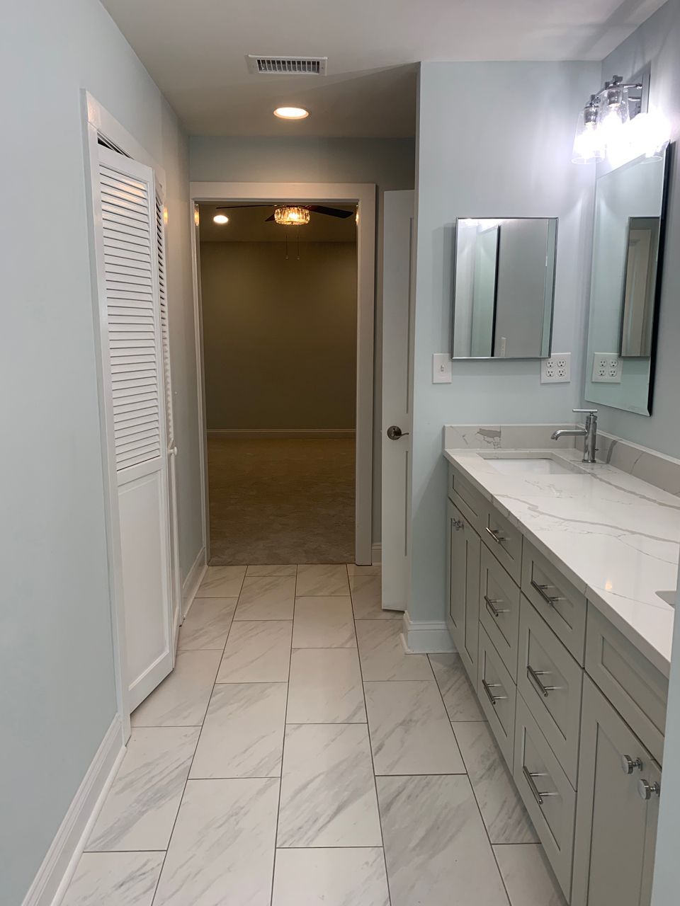 Bathroom with marble-look tile and light blue walls. A vanity with a mirror, cabinet, and a doorway.