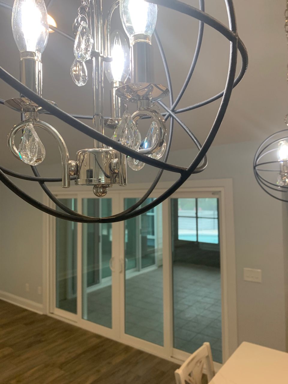 Chandelier over white-framed glass doors and windows overlooking a deck with brown flooring.