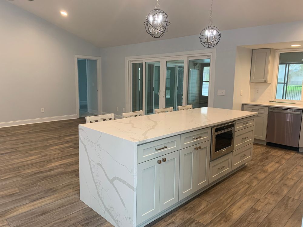 Modern kitchen with large island, light cabinets, quartz countertop, and wood-look floors.