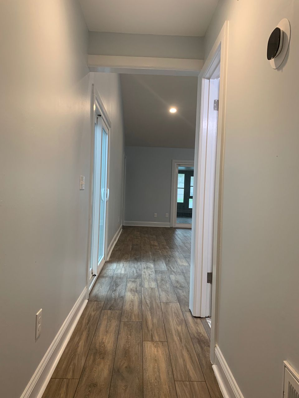 Narrow hallway with wood-look floors, light blue walls, and doorways leading to rooms.