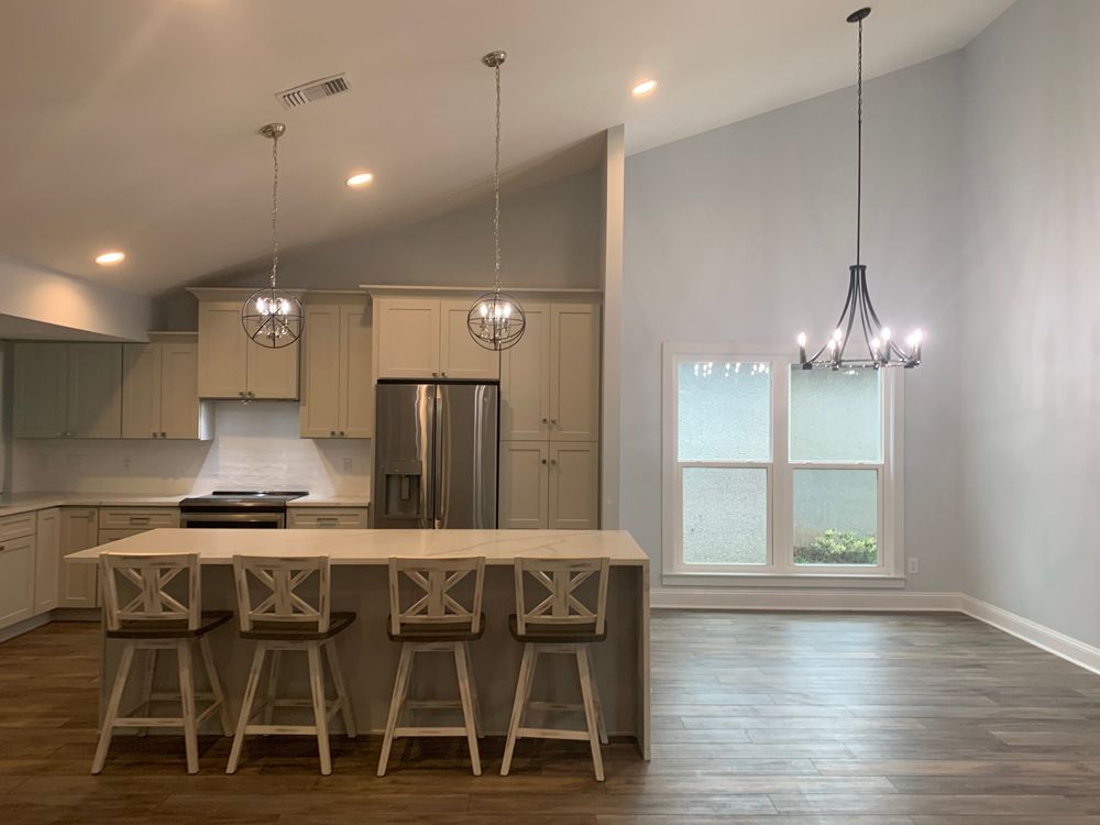 Spacious kitchen with light-colored cabinets, island with stools, stainless steel appliances, and high ceilings.