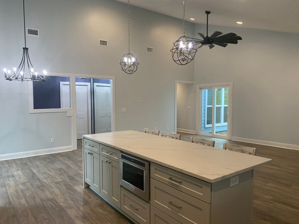 Kitchen with large island, light gray cabinets, light wood floors, high ceilings, and pendant lights.
