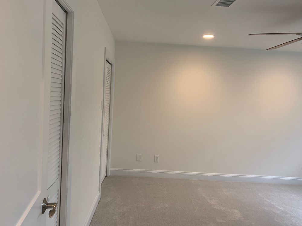 Empty white room with two doors, light carpet, and a ceiling fan.