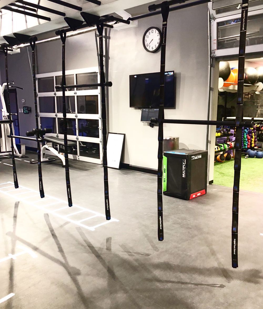 Gym interior with pull-up bars, a clock, TV, and a box for exercises. Concrete floor, glass door, and exercise equipment.