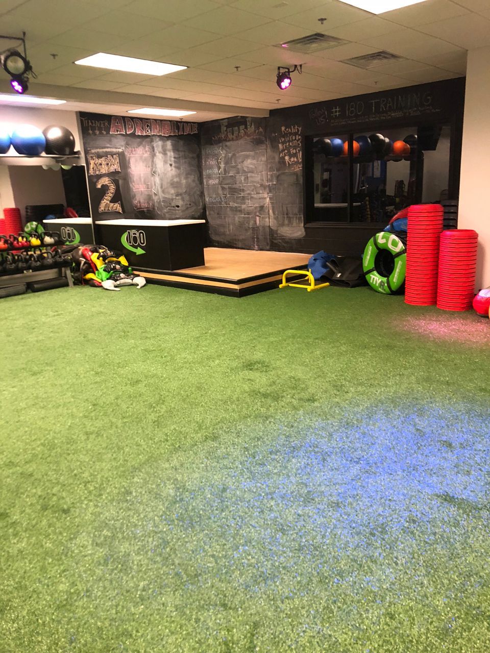 Gym interior with turf flooring, exercise equipment, and a small stage.