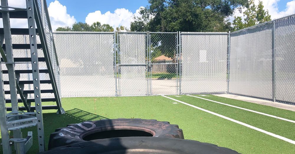 A fitness area with a chain-link fence, artificial turf, tires, and metal stairs.