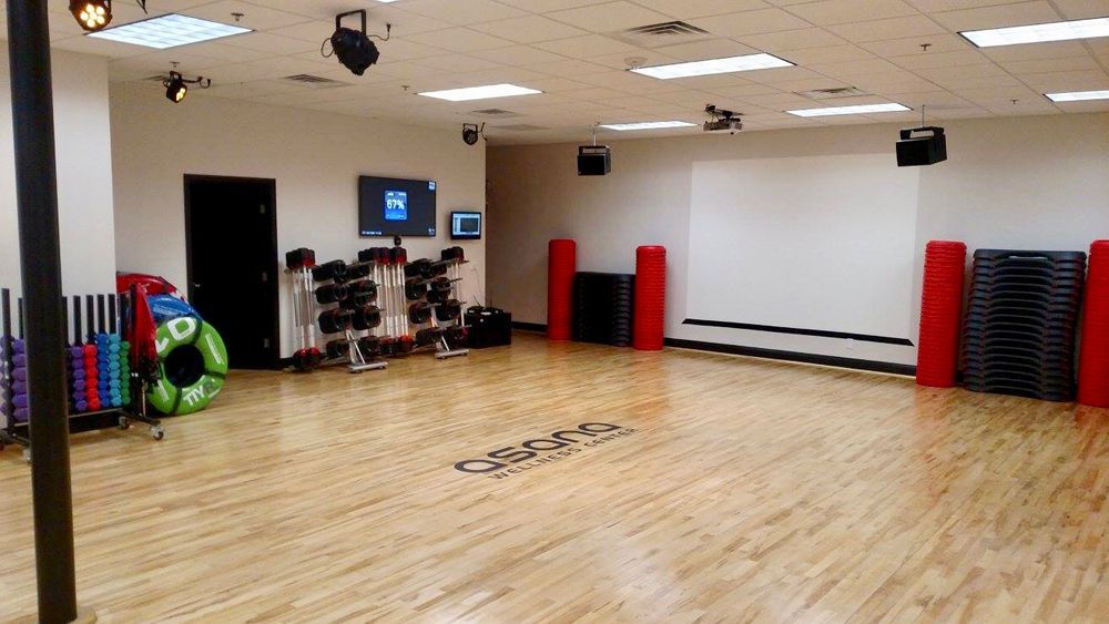 Empty gym with equipment, wood floor, and white wall.