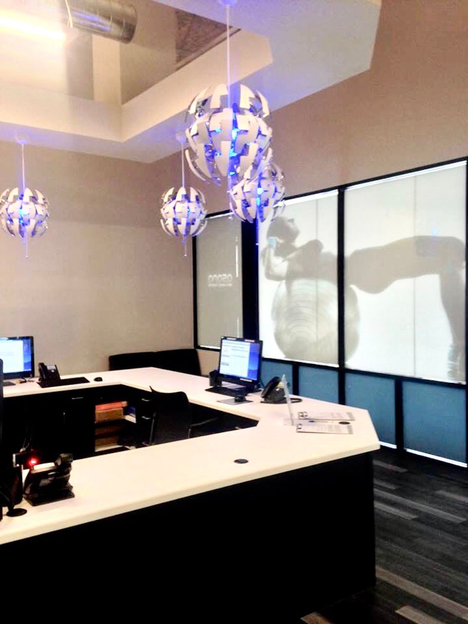 Office reception area with white and black desk, hanging globe lights, and silhouette-like images on the window panels.