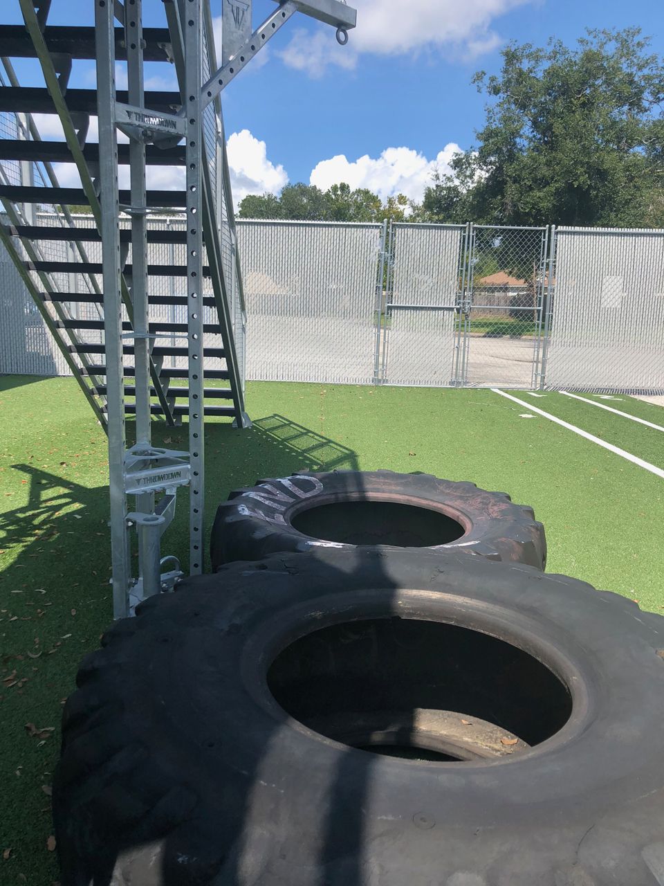 Two large tires on green turf near a metal staircase under a partly cloudy sky.