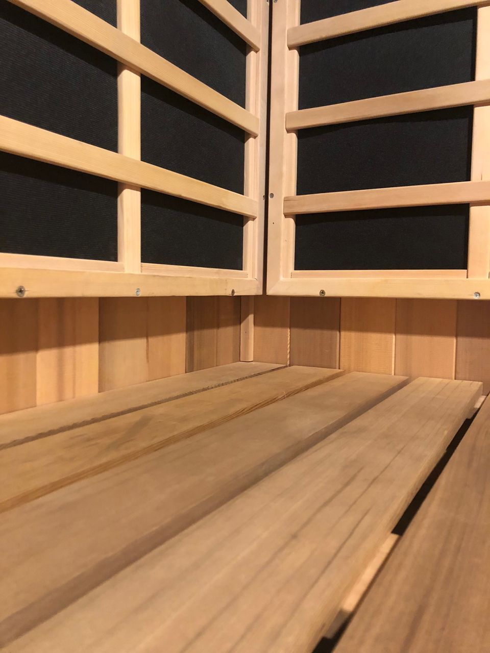 Inside of a sauna with wooden benches and walls, black insulation visible behind wood framework.
