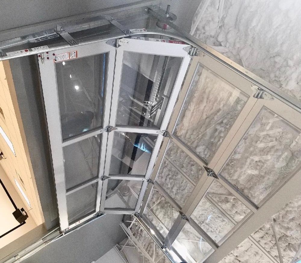 Glass and aluminum overhead garage door, partially open. The setting is an indoor space.