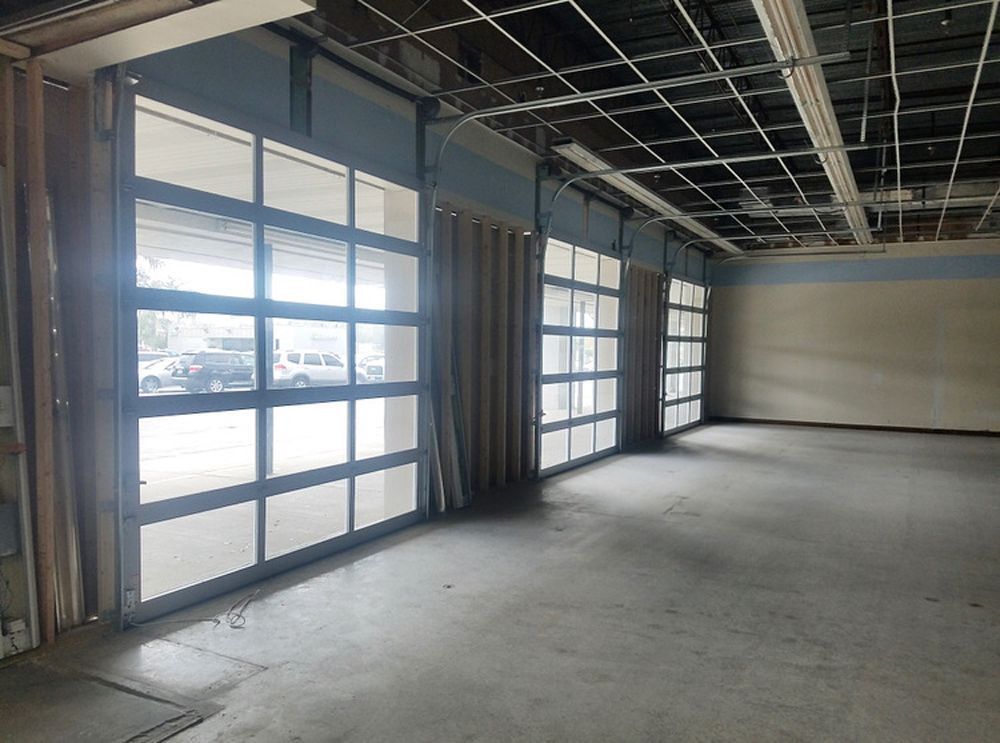 Interior of a room with large glass garage-style doors and unfinished ceiling. Empty with a concrete floor.