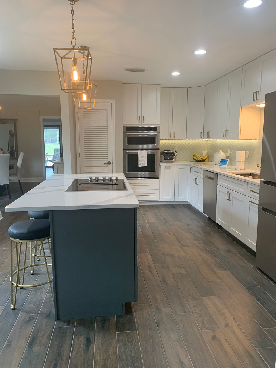 Modern kitchen with white cabinets, blue island, stainless steel appliances, and wood flooring.