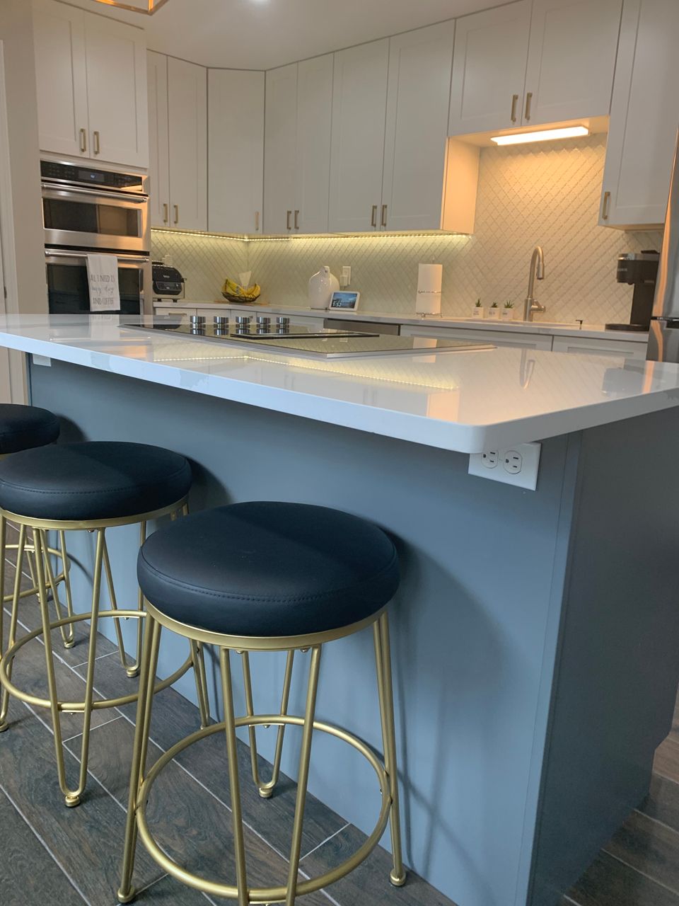 Modern kitchen with white cabinets, grey island, and gold stools.