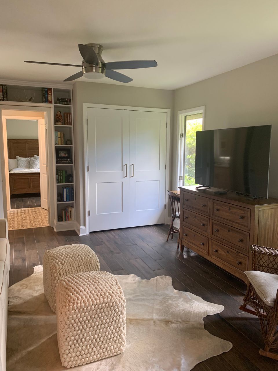 Living room with a cowhide rug, two woven ottomans, a wooden dresser, and a closet.