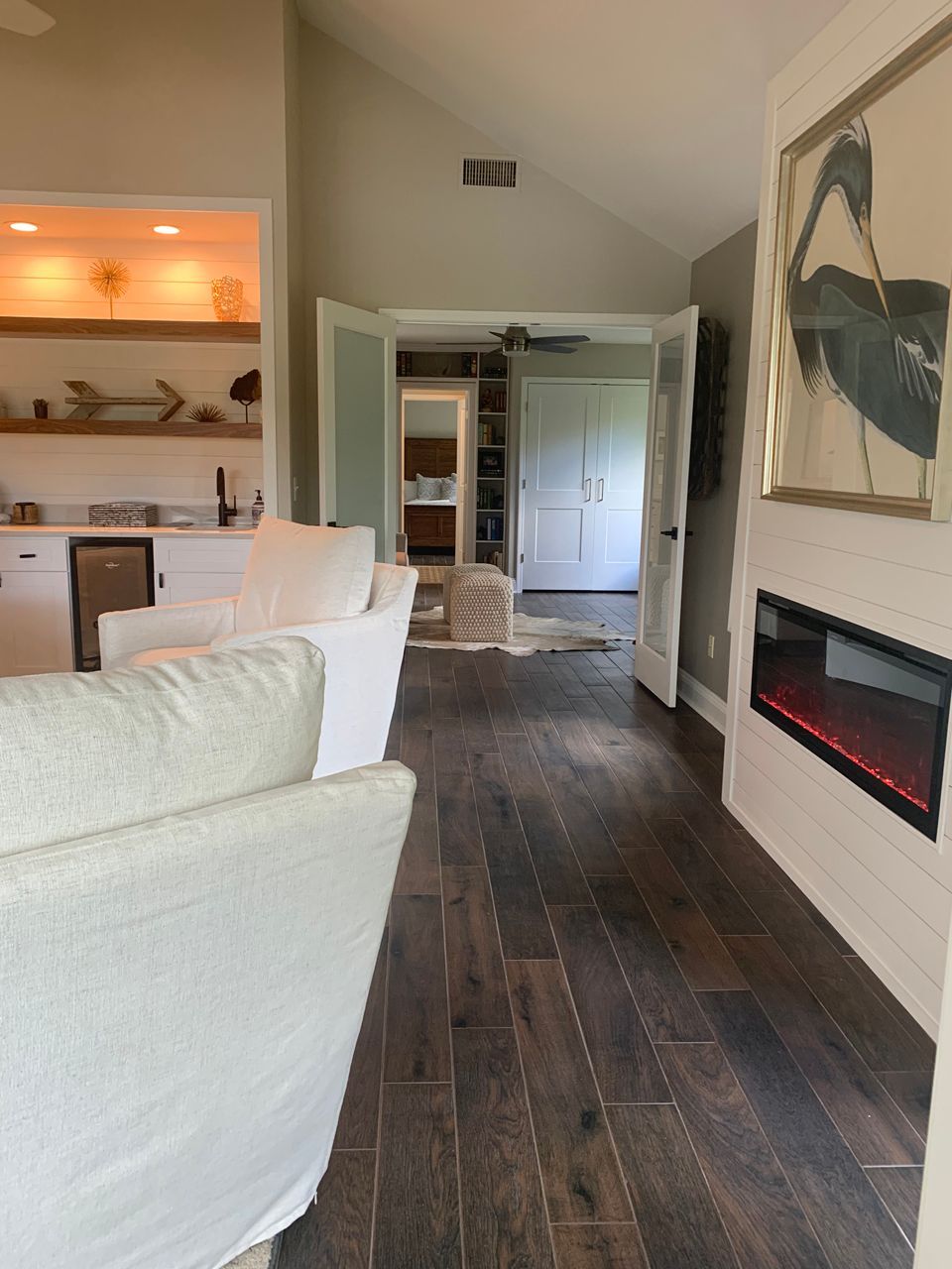 Living room with white furniture, dark wood floors, fireplace, and a view of a hallway.