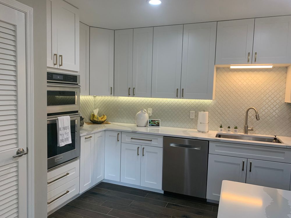 White kitchen with stainless steel appliances, white cabinets, and dark wood floors.