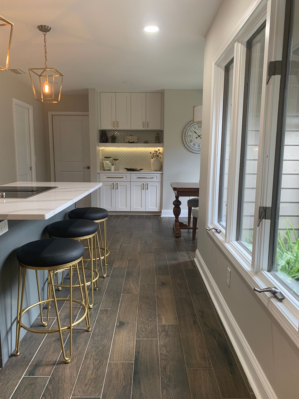 Kitchen with a gray island, gold stools, white cabinets, and wood flooring.