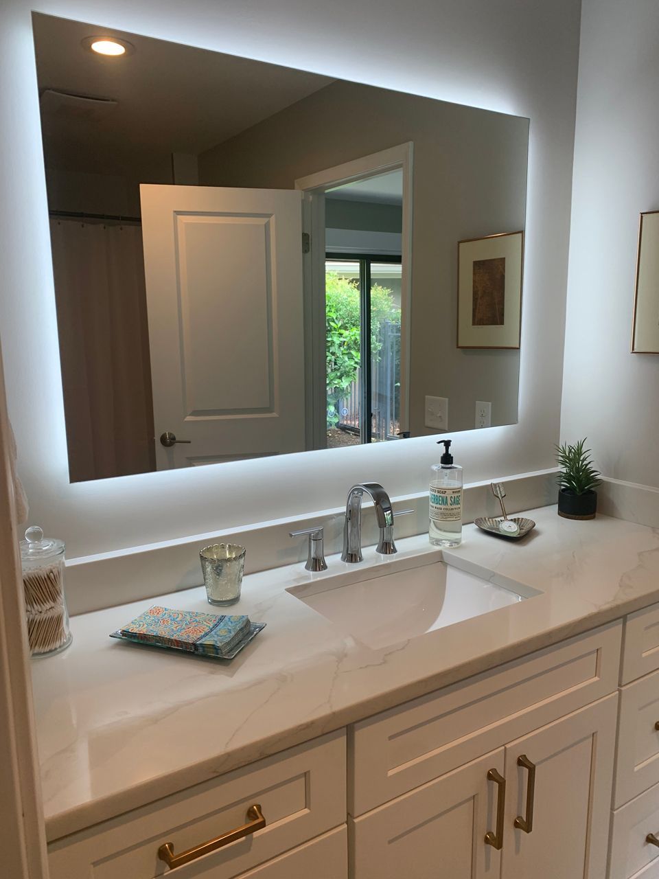 Bathroom with white vanity, rectangular mirror with LED lighting, and silver faucet.