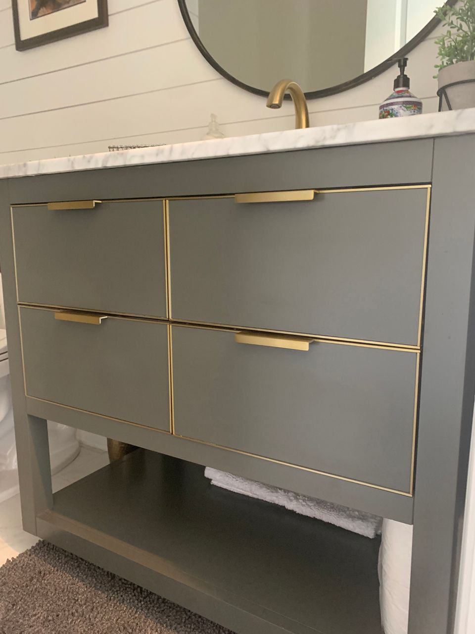 Gray bathroom vanity with gold trim and hardware, marble countertop, and round mirror.