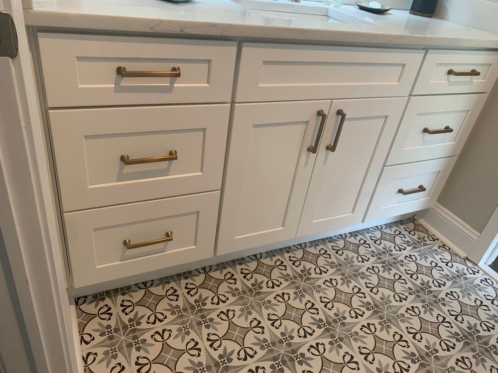 White bathroom vanity with gold hardware and patterned tile floor.