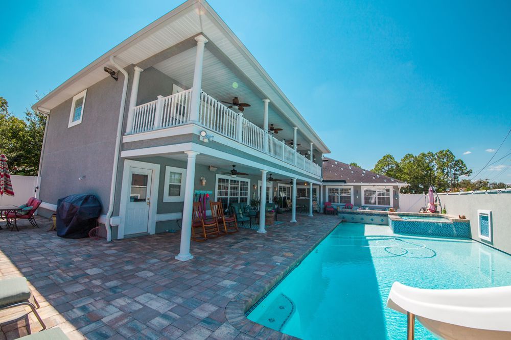 Two-story house with pool; gray exterior, white balconies. Blue sky, sunny day.