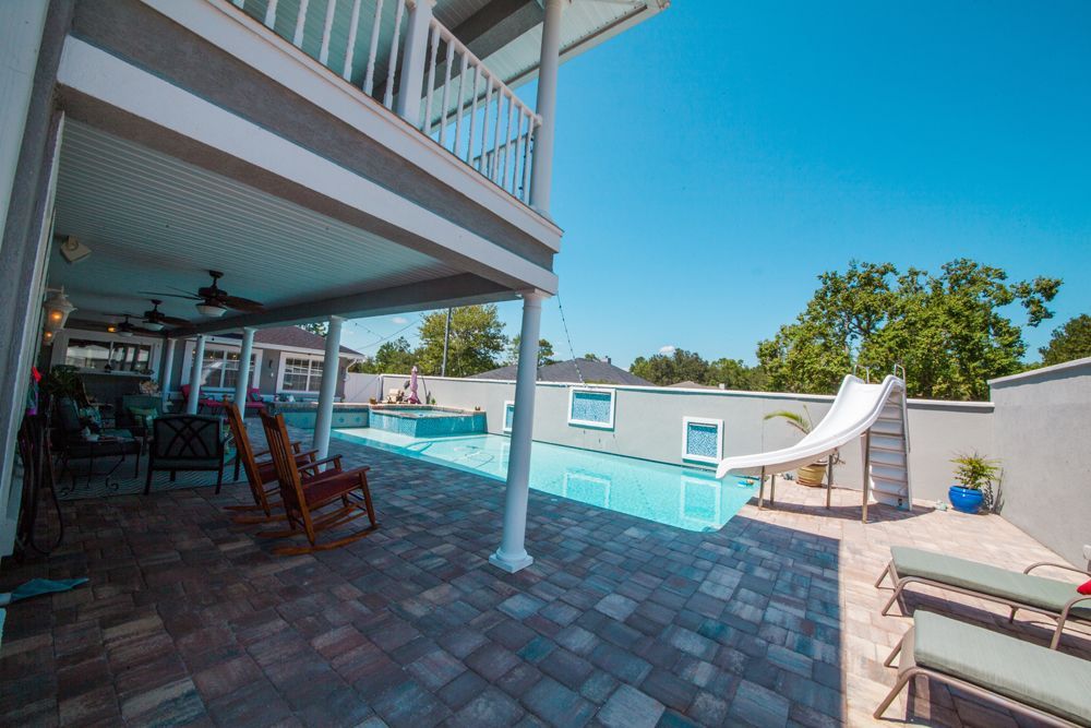 Backyard with a pool, patio, second-story balcony, and a water slide on a sunny day.