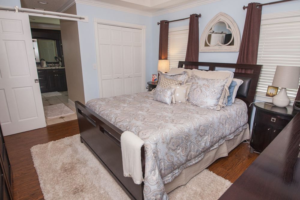 Bedroom with a bed, nightstands, and a doorway to a bathroom, light blue walls, brown wood floors.