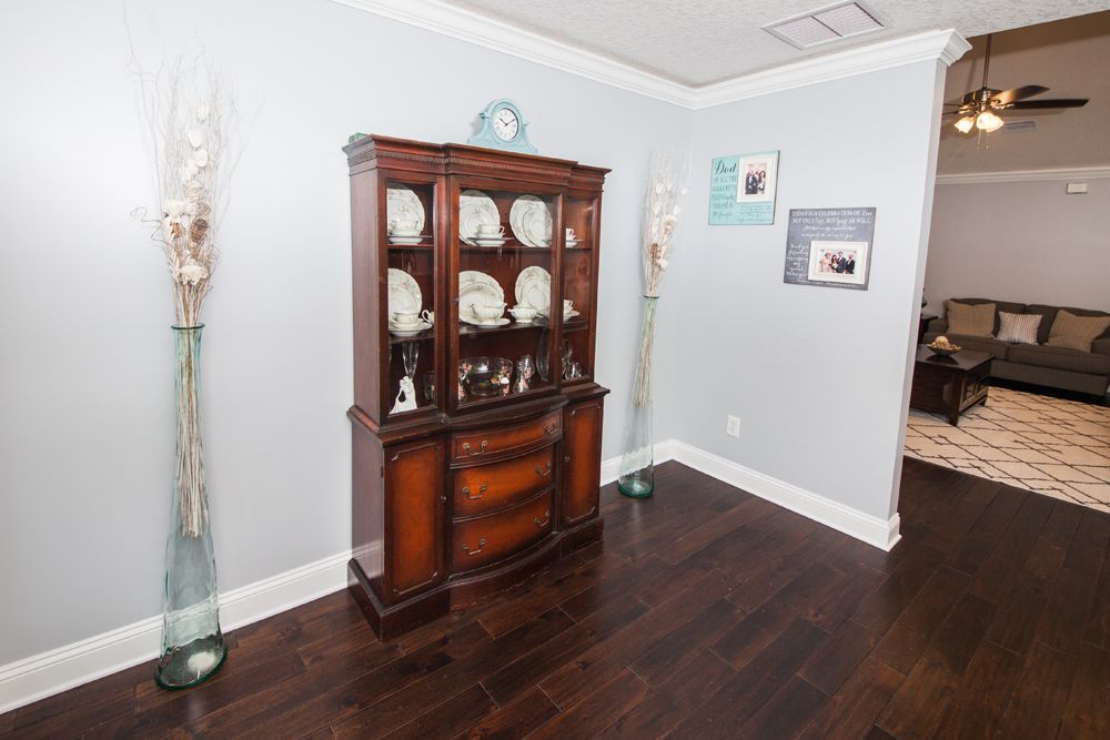 Dark wood hutch with white dishes, between two tall vases, in a room with dark wood floors.