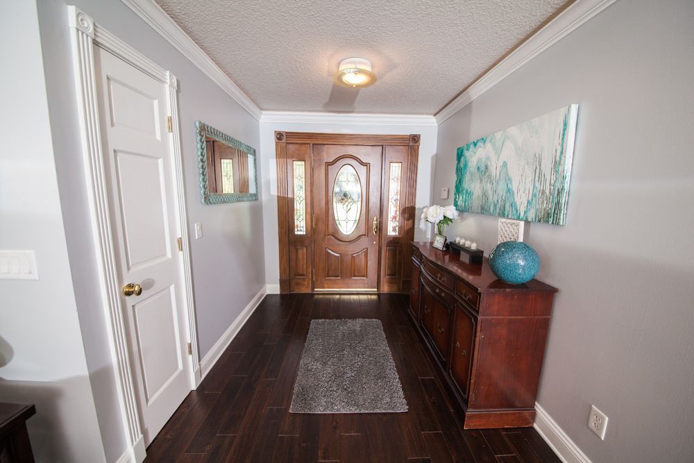Narrow hallway with dark wood floor, gray walls, a wooden door, and a console table with decor.