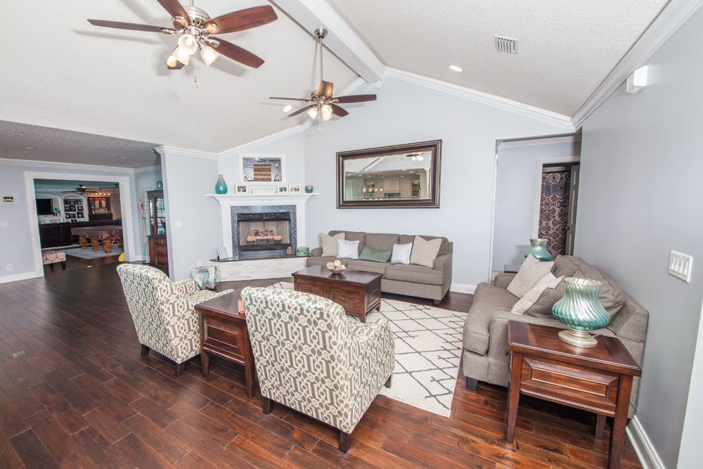 Spacious living room with fireplace, two patterned armchairs, brown sofa, and dark wood flooring.