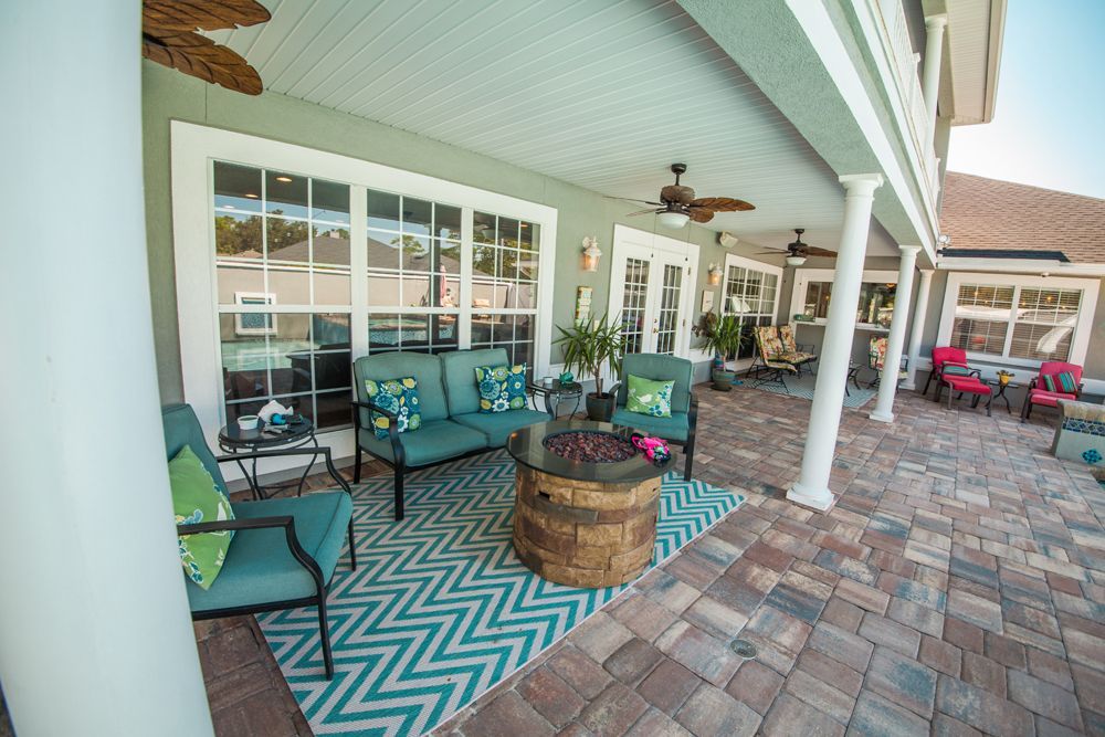 Patio with teal seating, fire pit, and patterned rug under a covered area with columns.