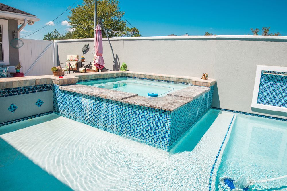 Pool with blue tile, waterfall spa, and pink umbrella on a sunny day.