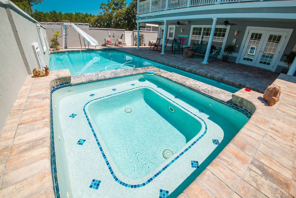 Pool and hot tub surrounded by brick patio, connected to a two-story house.