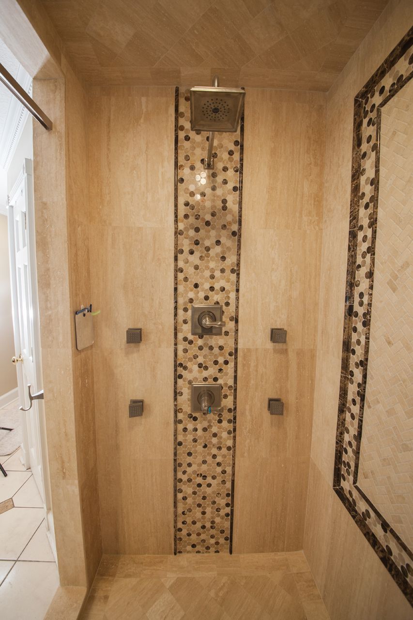 Tiled shower with a central, decorative mosaic strip.  Neutral colors, multiple showerheads.