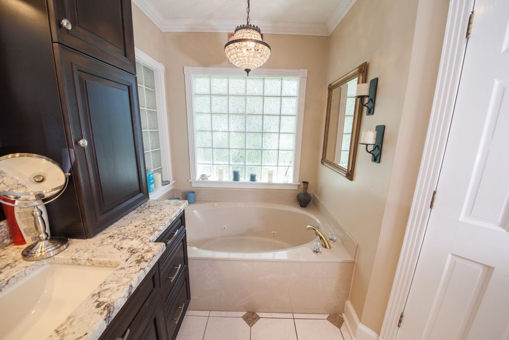 Bathroom with a bathtub, vanity with dark cabinetry, a window, and a chandelier.