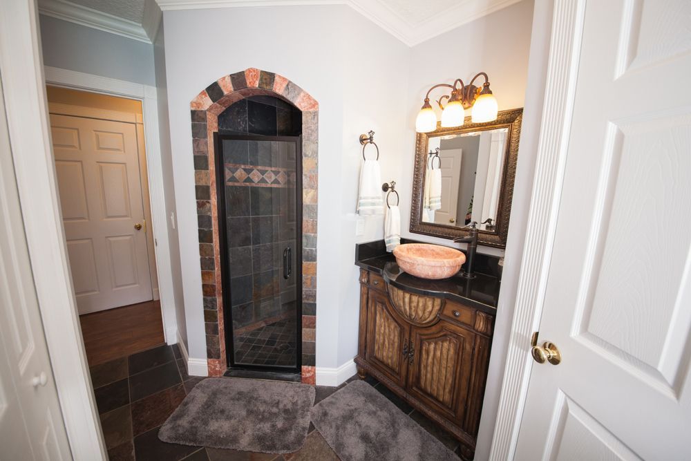 Bathroom with a shower, vanity, and doorway. The shower has a brick-lined arch.