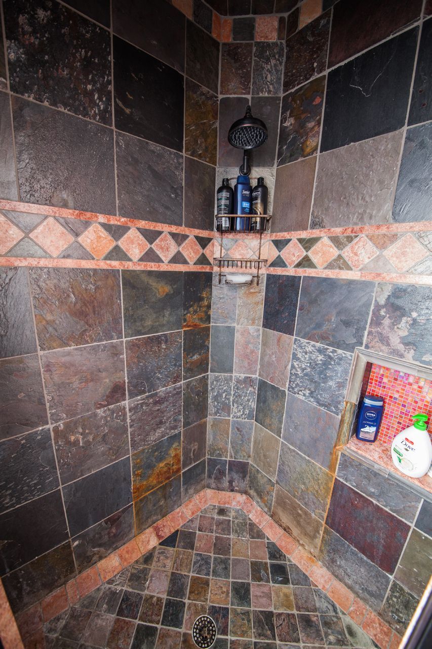 Shower with multi-colored slate tiles, a decorative band, and a built-in shelf holding toiletries.
